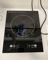 Top view of the induction cooker showing the smooth black glass surface with control icons and circular cooking zone.