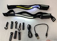 Two black induction headlamps lit to show LED light strips with multiple black mounting clips and two USB charging cables.