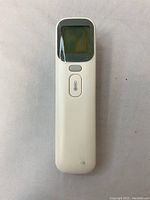 Front view of white infrared thermometer with display screen covered in protective film and single button below it.