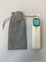 Infrared thermometer next to grey drawstring pouch against a white background