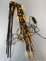 Two closely viewed images of the same LED faux branch lights set showing warm white LED bulbs lit along dark brown faux branches with a visible inline power switch on the cord.
