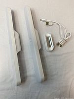 Two white LED mirror lights with magnetic mounts and USB cable lying side by side on fabric surface, showing physical condition and included accessories.