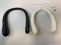 Front view of two neck fans, black and white models, shown side by side with USB charging cords attached.