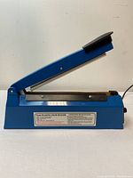 Side view of blue plastic film sealer showing handle and front sealing area with operating instructions label.