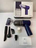 Photo of handheld vacuum cleaner with box, attachments, charging cable, and manual