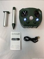 Solar Animal Repeller main unit with control dials, ultrasonic speakers, motion sensor, and lit LEDs, displayed with mounting stake parts, USB charging cable, and user manual on white background.