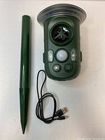 Green solar-powered animal repellent device with 360 degree sensor and lights, shown with spike mount stake and USB charging cable.