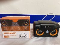 Photo of the QueenMew Ultrasonic Bark Control device next to its orange and black packaging showing the front device design and product features.