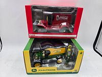 Two boxed 1:24 diecast model vehicles, one Coca-Cola truck and one John Deere delivery car with a gas pump.