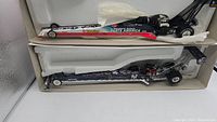 Two 1:24 scale diecast Top Fuel dragsters displayed in original packaging with styrofoam support and tissue paper, showing overall condition and packaging.