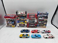 Photo of 18 NASCAR 1:64 scale diecast cars with several in original boxes and some loose cars arranged in front.