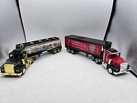 Two collectible semi truck toys side by side: a black and gold Texaco tanker truck and a red and black Marvel Oil Co. semi truck.