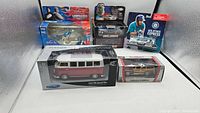 Photo showing 1957 VW Classic Bus 1:25 diecast model in packaging along with other boxed diecast items in a lit display case.