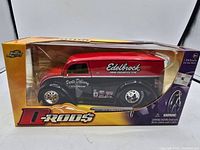 Front angled view of the boxed Jada 1:24 scale D Rods die-cast vehicle, showing black and red hot rod with Edelbrock decals, in sealed packaging.