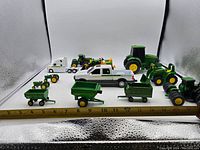 Wide view of all toys in lot showing various John Deere tractors, trailers, a pickup truck, and farm equipment models lined up with measuring scale.