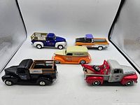 Photo of five 1:24 scale diecast trucks showing their side and top profiles, featuring various colors and detailing, with one truck visibly having a broken front bumper.