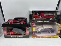 Four diecast vehicles in original boxes. Back row: red 1929 Mack firetruck and black Parts Plus van. Front row: red firetruck and purple/gray Car Quest 37 Chevy Sedan.