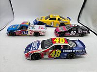 Four NASCAR diecast cars shown together - three 1:24 scale including #48 Lowe's Jimmy Johnson, #98 Raybestos truck, #99 Exide car, and one 1:18 scale #1 Moog Racing car in yellow and blue.