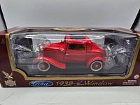 Front angle side view of the 1932 Ford diecast model in original box, showing clear packaging and red car body with white wall tires.