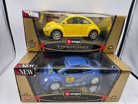 Two Bburago Volkswagen 1:18 scale diecast car models in original packaging, one yellow Volkswagen New Beetle and one blue Volkswagen race car.