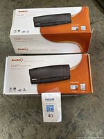 Two Ambir DS687 Card Scanner boxes stacked with Maxsold lot tag visible, showing branding and product image.