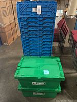 Stack of blue crates behind two green bins on concrete floor