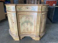 Front view of curved decorative cabinet with detailed painted botanical designs and gold trim.