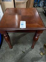 Full view of the brown wooden end table showing square top and turned legs with some scratches and surface wear.