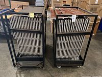 Two black steel racks each loaded with multiple square wood flooring panels