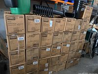 Multiple stacked cardboard boxes each containing 12 Rubbermaid Side Bins, model 2950, totaling approximately 60 units.