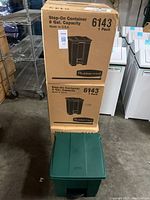 Boxed Rubbermaid Step-On container with 8 gallon capacity and a green container with closed lid in front