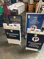 Four plasticade signs placed together showing various clinic and COVID testing information with handles visible.