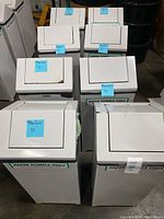 Eight white trash bins with swivel top lids arranged indoors, each with a label "PAPER TOWELS ONLY" showing slight usage wear.