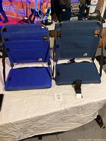 Two bleacher seats, one navy blue and one blue, placed on a table showing fabric and straps