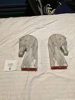 Pair of horse head shaped marble book ends lying on fabric surface, showing front and side views.