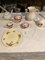 Assorted china items including teapots, creamers, plate, pitcher arranged on white cloth