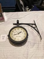 Photo of double-sided wall clock with "Grand Central Terminal New York" face, black metal frame and bracket on white surface.