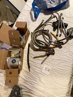 Overview of construction supplies including several flexible metal hoses, pliers, a segmented drill bit extension, punch tool, and opened boxes with door holder parts.