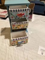 Full front view of the decorative drawer unit showing the three porcelain drawers with colorful floral design and striped top edges, handles on the drawers are red, yellow, and blue.