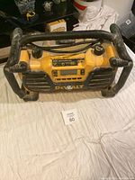 Front view of Dewalt DC012 jobsite radio showing control panel, digital display, and black protective roll cage surrounding yellow body.