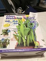 Box of Glass Watering Sphere Deluxe, showing front side with pictures and text describing use and features.