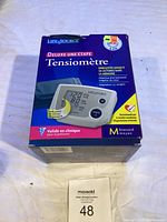Front of the LifeSource Deluxe One-Step Blood Pressure Monitor box showing product image and description in French and English. Model includes medium cuff and memory for 90 readings.