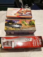 Three boxed kitchen supply items on a white tablecloth: Nicodicer chopper, Supreme Dicer, and Betty Crocker Hand Blender.