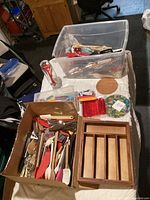 Photo showing two containers filled with various kitchen utensils including spatulas, whisks, tongs, and peelers along with a wooden utensil drawer organizer on a table.