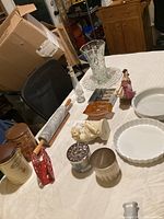 Photo showing a variety of kitchenware and decorative items including glass vase, rolling pins, ceramic dishes, and figurines on a white surface.