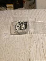 Plastic clear container filled with small black and white bobbin-shaped magnets placed on a white cloth.