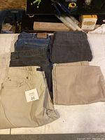 Four pairs of folded pants lying on a surface, colors include blue, black, dark grey denim, and beige.