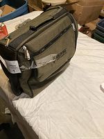 Closed front view of olive green textured fabric picnic bag with black trim and multiple zippered compartments