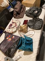 Lot of 7 purses arranged on a bed, showing various colors and styles