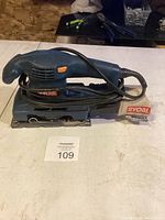 Ryobi electric sander with power cord coiled on top, showing overall condition and details.